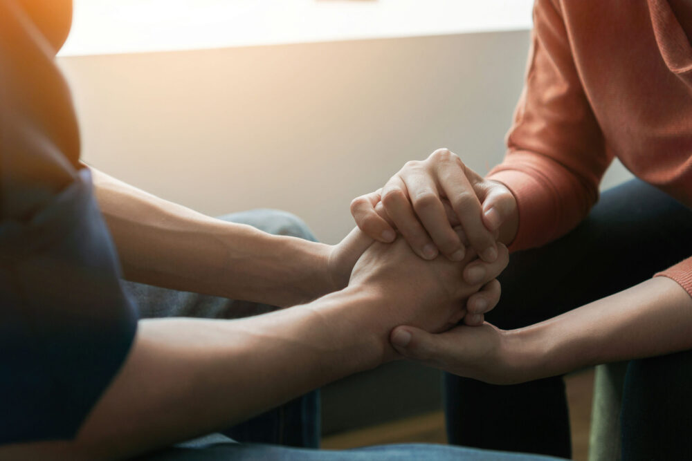 Two people holding hands during a supportive counseling session demonstrating therapy benefits to mental health.