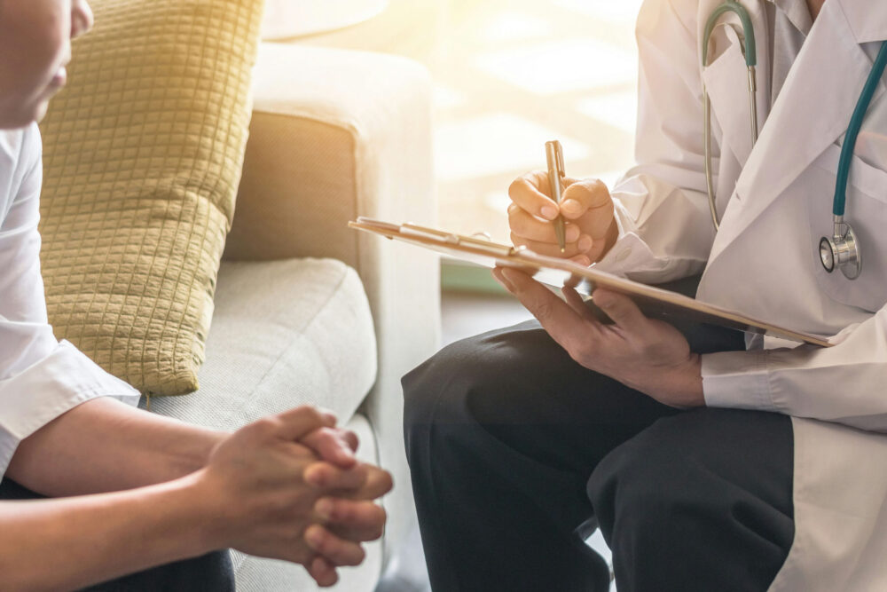 Doctor taking notes while speaking with patient during counseling session highlighting therapy benefits to mental health.
